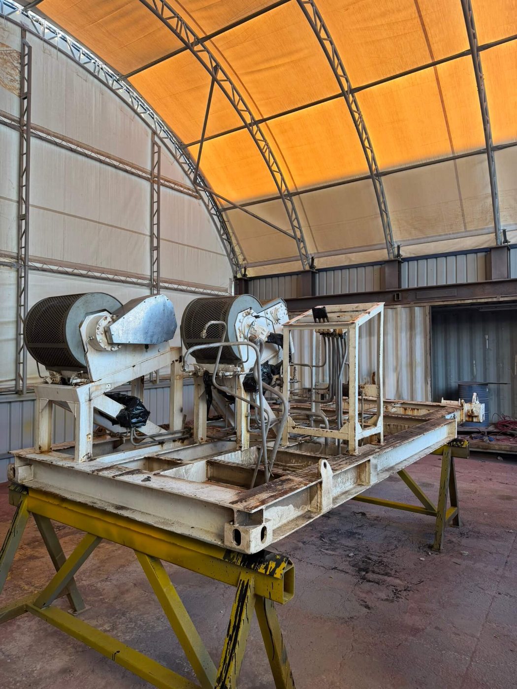 Plant skid with peeling cream coating, oil residue and rust across the base frame and drum housings before blasting
