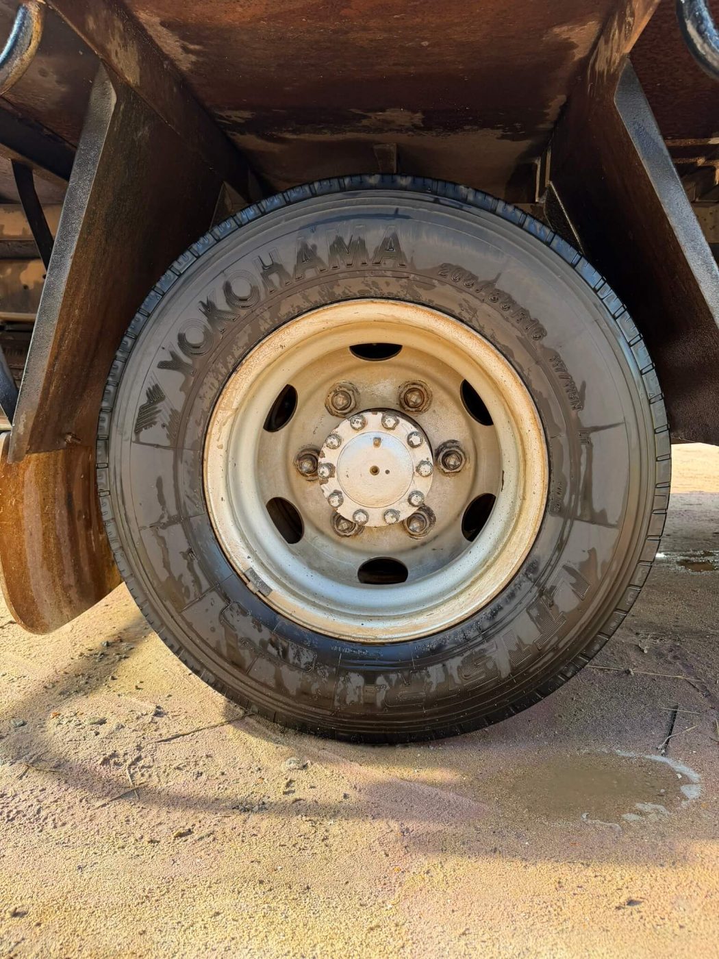 Truck rim with stained, chipped paint and rust around the hub and wheel nuts before blasting