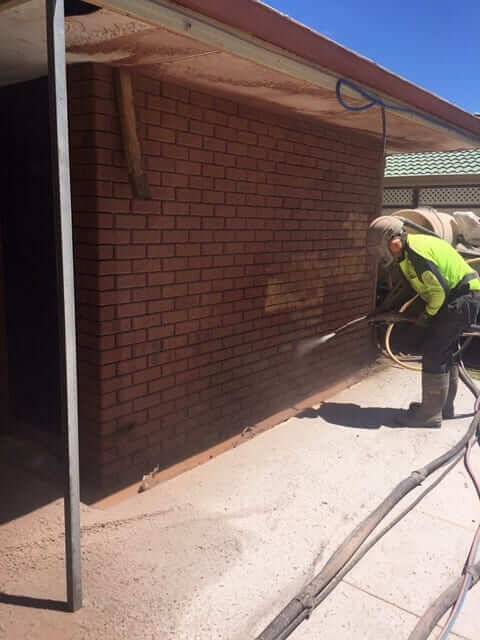 Blaster removing paint from a red brick house wall in Perth