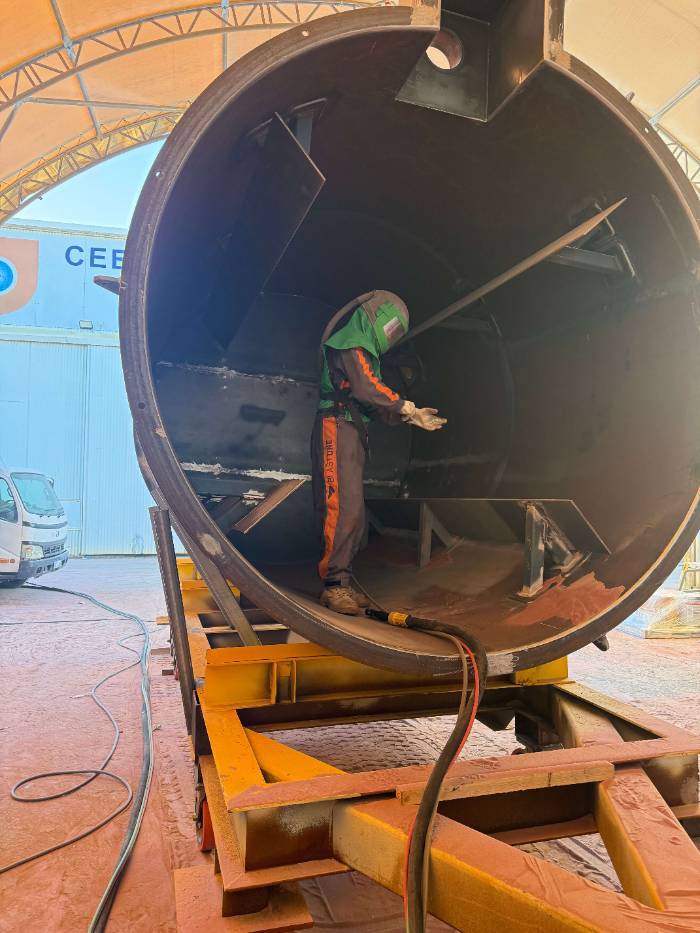 Blaster working inside a large steel tank shell under a WA containment tent